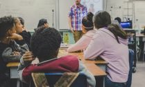 Students seated at desks in a diverse classroom, listening to a teacher standing at the front near a whiteboard. Children of Hope Initiative